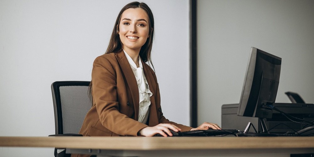 Funcionária sorrindo enquanto trabalha em frente a um computador, representando a eficiência das dicas de produtividade