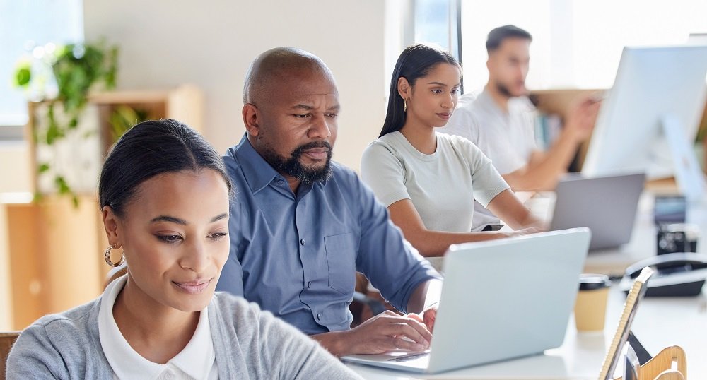 Grupo de colaboradores trabalhando em laptops com acesso a um plano de internet para empresas.