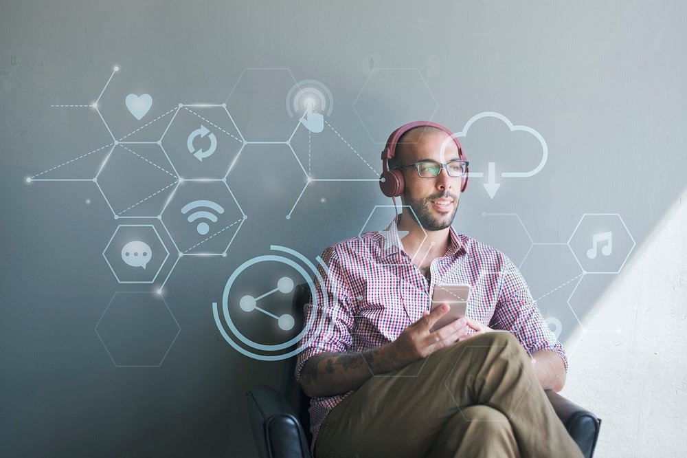 Imagem de um homem sentado com o celular na mão, pensando em vários assuntos de tecnologia.