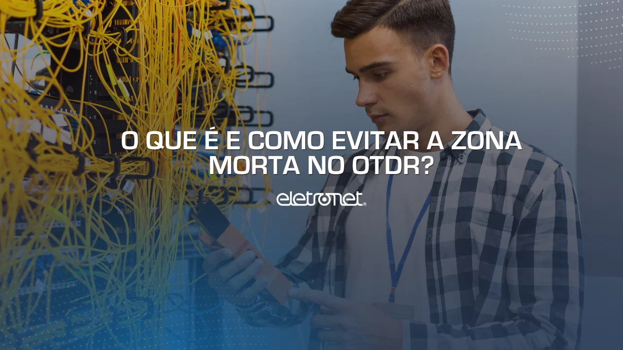 Homem branco com OTDR na mão medindo a zona morta da fibra óptica ao lado de um emaranhado de cabos amarelos.